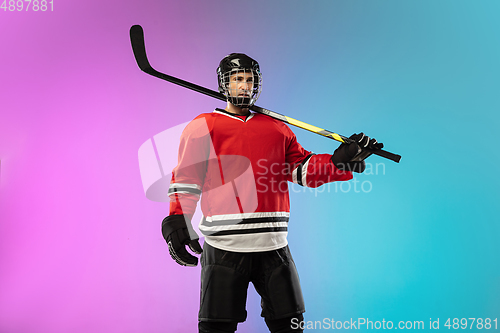 Image of Male hockey player with the stick on ice court and neon colored gradient background. Sportsman wearing equipment, helmet practicing.