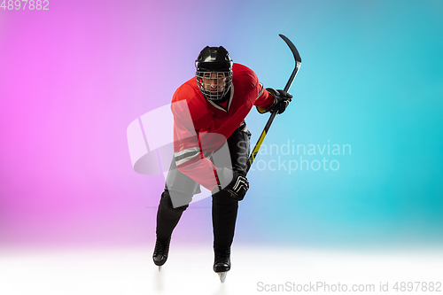 Image of Male hockey player with the stick on ice court and neon colored gradient background. Sportsman wearing equipment, helmet practicing.