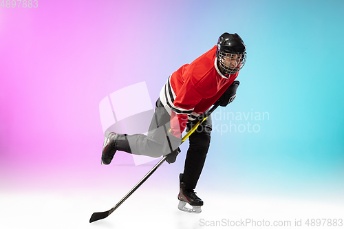 Image of Male hockey player with the stick on ice court and neon colored gradient background. Sportsman wearing equipment, helmet practicing.