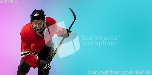 Image of Male hockey player with the stick on ice court and neon colored gradient background. Sportsman wearing equipment, helmet practicing.
