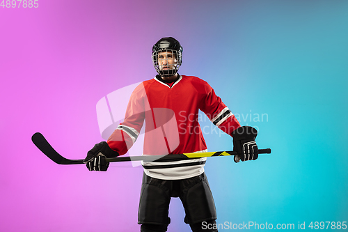 Image of Male hockey player with the stick on ice court and neon colored gradient background. Sportsman wearing equipment, helmet practicing.