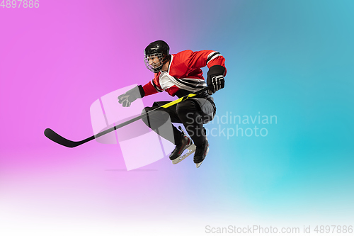 Image of Male hockey player with the stick on ice court and neon colored gradient background. Sportsman wearing equipment, helmet practicing.