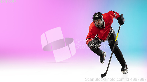 Image of Male hockey player with the stick on ice court and neon colored gradient background. Sportsman wearing equipment, helmet practicing.