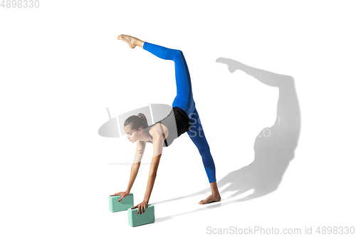 Image of Beautiful young female athlete stretching on white studio background with shadows