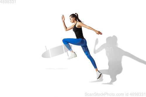 Image of Beautiful young female athlete stretching on white studio background with shadows