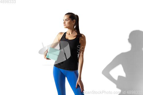 Image of Beautiful young female athlete stretching on white studio background with shadows