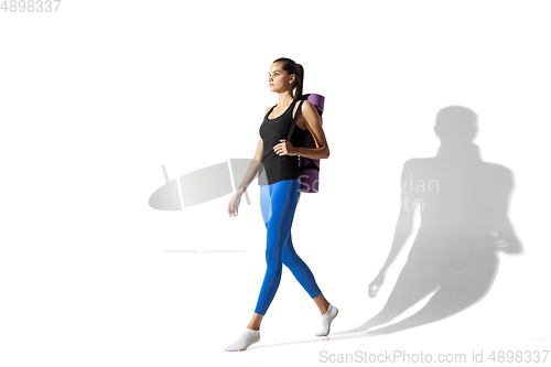 Image of Beautiful young female athlete stretching on white studio background with shadows