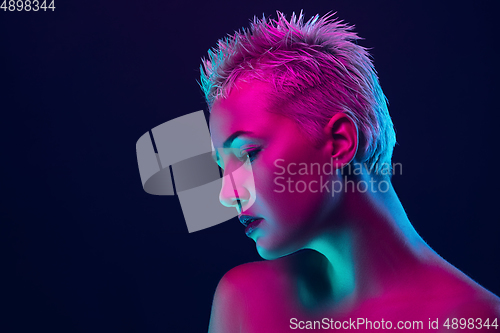 Image of Portrait of female fashion model in neon light on dark studio background.