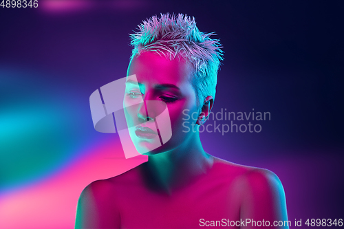 Image of Portrait of female fashion model in neon light on dark studio background.