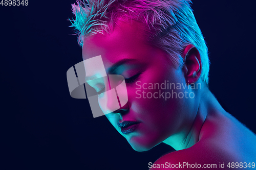 Image of Portrait of female fashion model in neon light on dark studio background.