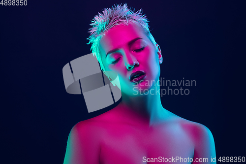 Image of Portrait of female fashion model in neon light on dark studio background.