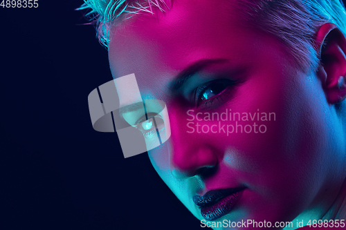 Image of Portrait of female fashion model in neon light on dark studio background.