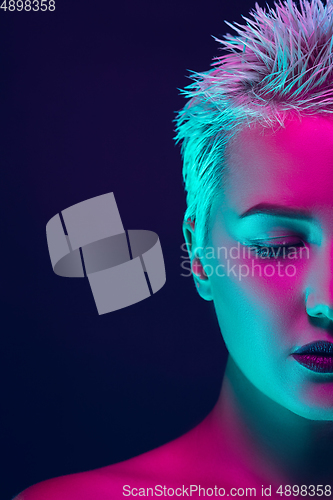 Image of Portrait of female fashion model in neon light on dark studio background.