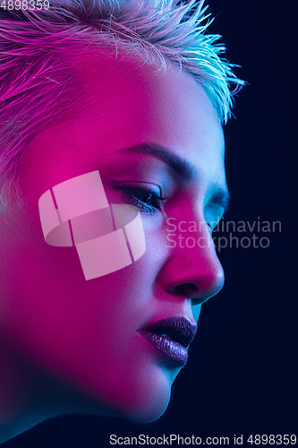 Image of Portrait of female fashion model in neon light on dark studio background.