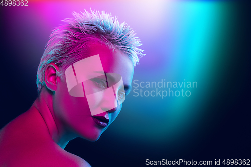 Image of Portrait of female fashion model in neon light on dark studio background.
