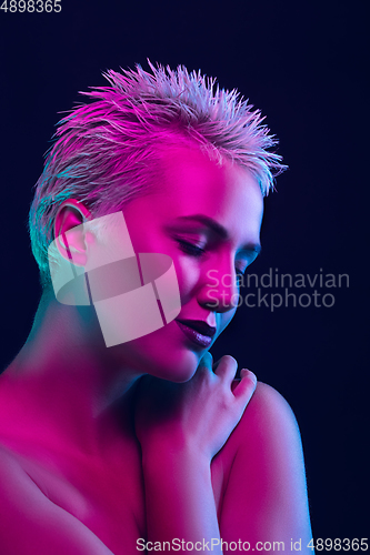 Image of Portrait of female fashion model in neon light on dark studio background.