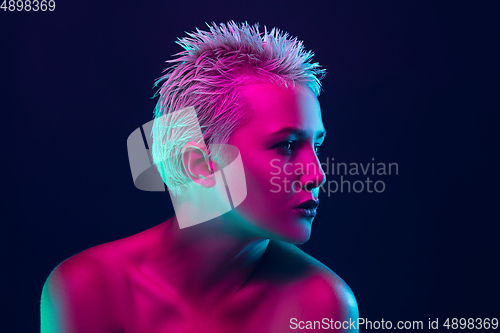 Image of Portrait of female fashion model in neon light on dark studio background.