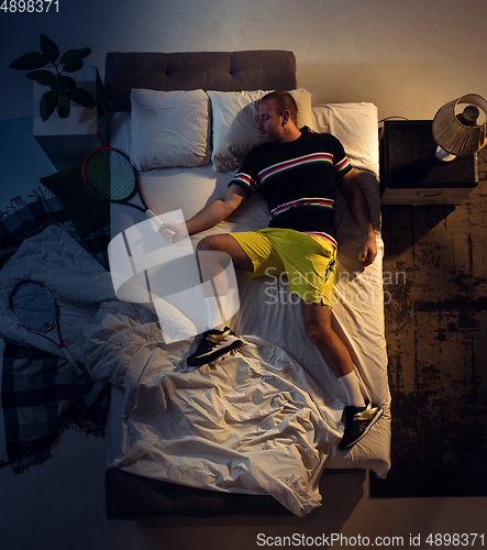 Image of Top view of young professional tennis player sleeping at his bedroom in sportwear with racket