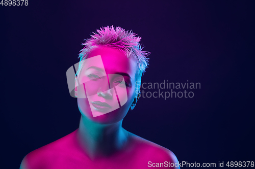 Image of Portrait of female fashion model in neon light on dark studio background.