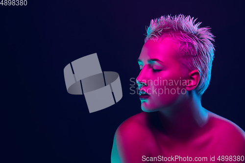 Image of Portrait of female fashion model in neon light on dark studio background.