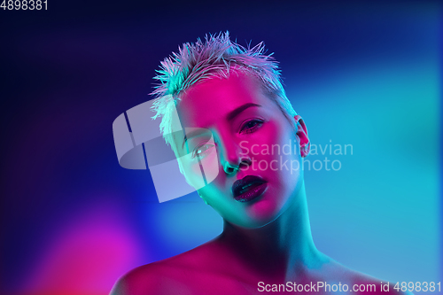 Image of Portrait of female fashion model in neon light on dark studio background.