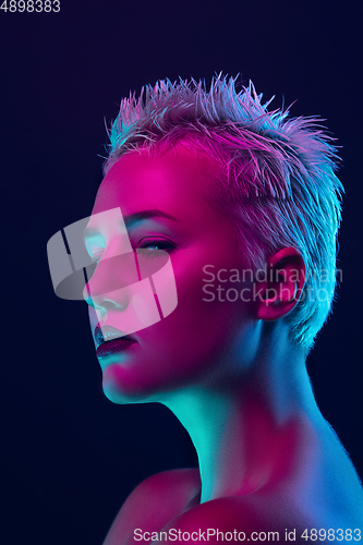 Image of Portrait of female fashion model in neon light on dark studio background.