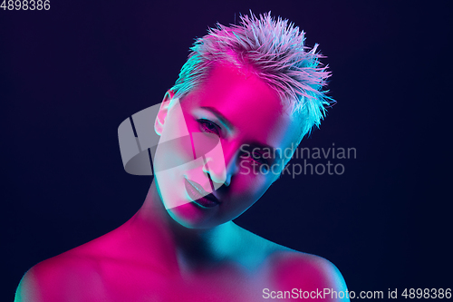 Image of Portrait of female fashion model in neon light on dark studio background.