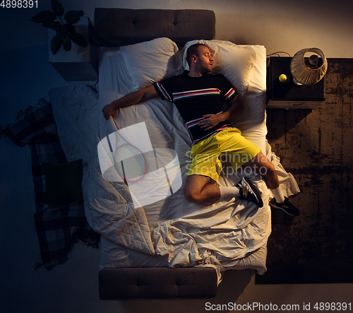 Image of Top view of young professional tennis player sleeping at his bedroom in sportwear with racket