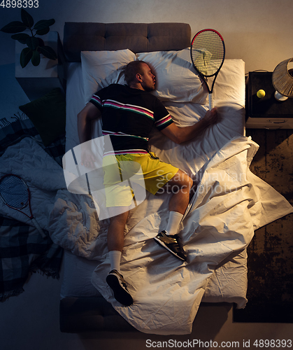 Image of Top view of young professional tennis player sleeping at his bedroom in sportwear with racket