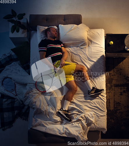 Image of Top view of young professional tennis player sleeping at his bedroom in sportwear with racket