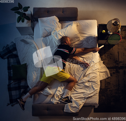 Image of Top view of young professional tennis player sleeping at his bedroom in sportwear with racket