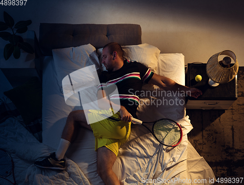 Image of Top view of young professional tennis player sleeping at his bedroom in sportwear with racket