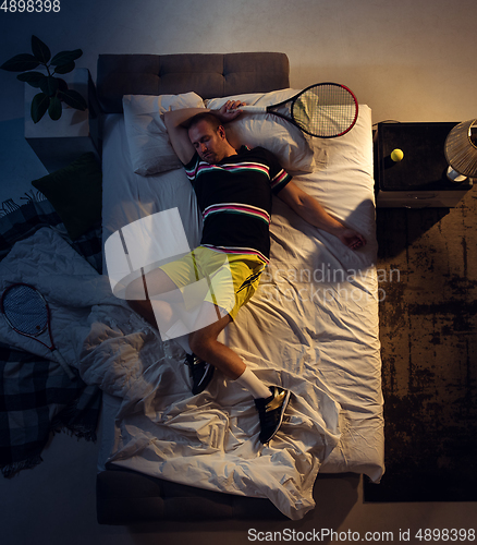 Image of Top view of young professional tennis player sleeping at his bedroom in sportwear with racket