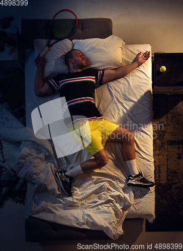 Image of Top view of young professional tennis player sleeping at his bedroom in sportwear with racket