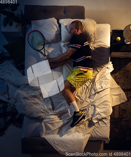 Image of Top view of young professional tennis player sleeping at his bedroom in sportwear with racket