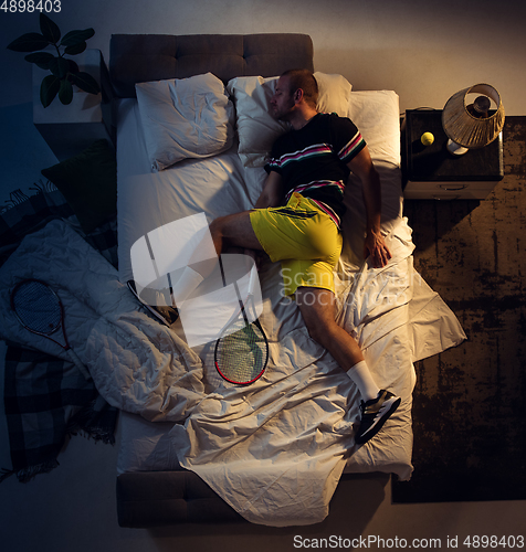 Image of Top view of young professional tennis player sleeping at his bedroom in sportwear with racket