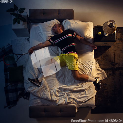 Image of Top view of young professional tennis player sleeping at his bedroom in sportwear with racket