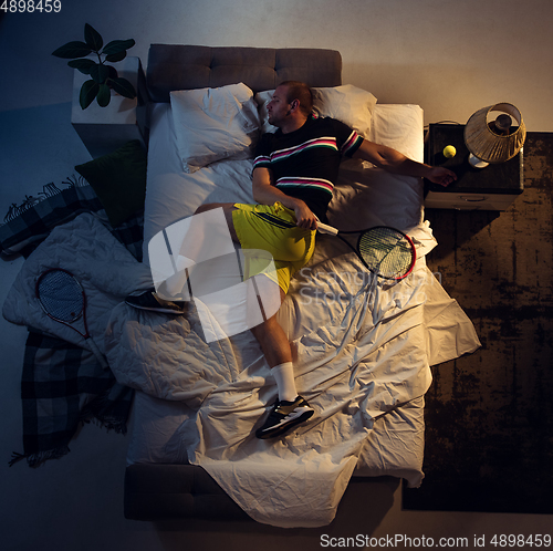 Image of Top view of young professional tennis player sleeping at his bedroom in sportwear with racket