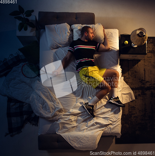 Image of Top view of young professional tennis player sleeping at his bedroom in sportwear with racket