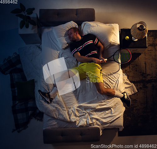 Image of Top view of young professional tennis player sleeping at his bedroom in sportwear with racket