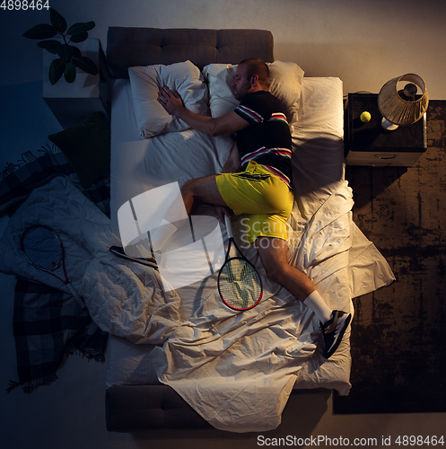 Image of Top view of young professional tennis player sleeping at his bedroom in sportwear with racket