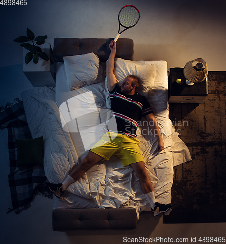 Image of Top view of young professional tennis player sleeping at his bedroom in sportwear with racket