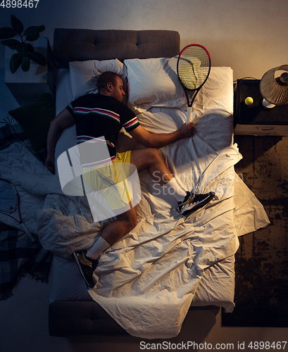 Image of Top view of young professional tennis player sleeping at his bedroom in sportwear with racket