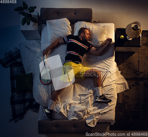 Image of Top view of young professional tennis player sleeping at his bedroom in sportwear with racket