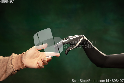 Image of Hand of Santa Muerte, Saint death or Sugar skull with bright make-up touching human hand isolated on dark green background like touch of God