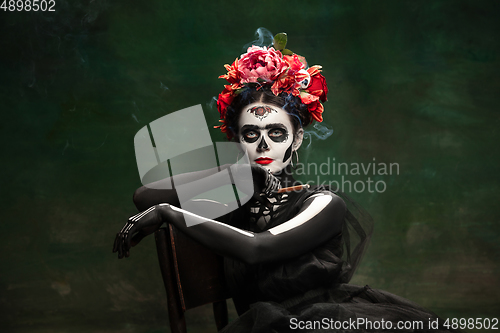 Image of Young girl in the image of Santa Muerte, Saint death or Sugar skull with bright make-up. Portrait isolated on studio background.