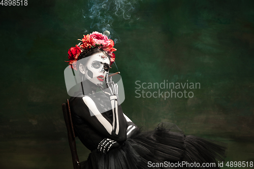 Image of Young girl in the image of Santa Muerte, Saint death or Sugar skull with bright make-up. Portrait isolated on studio background.