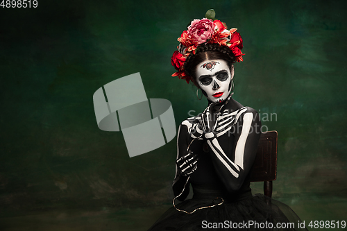 Image of Young girl in the image of Santa Muerte, Saint death or Sugar skull with bright make-up. Portrait isolated on studio background.