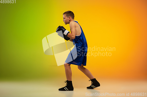 Image of Teenage boxer against gradient neon studio background in motion of kicking, boxing