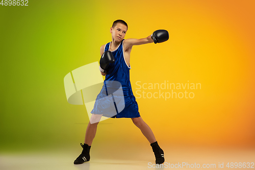 Image of Teenage boxer against gradient neon studio background in motion of kicking, boxing